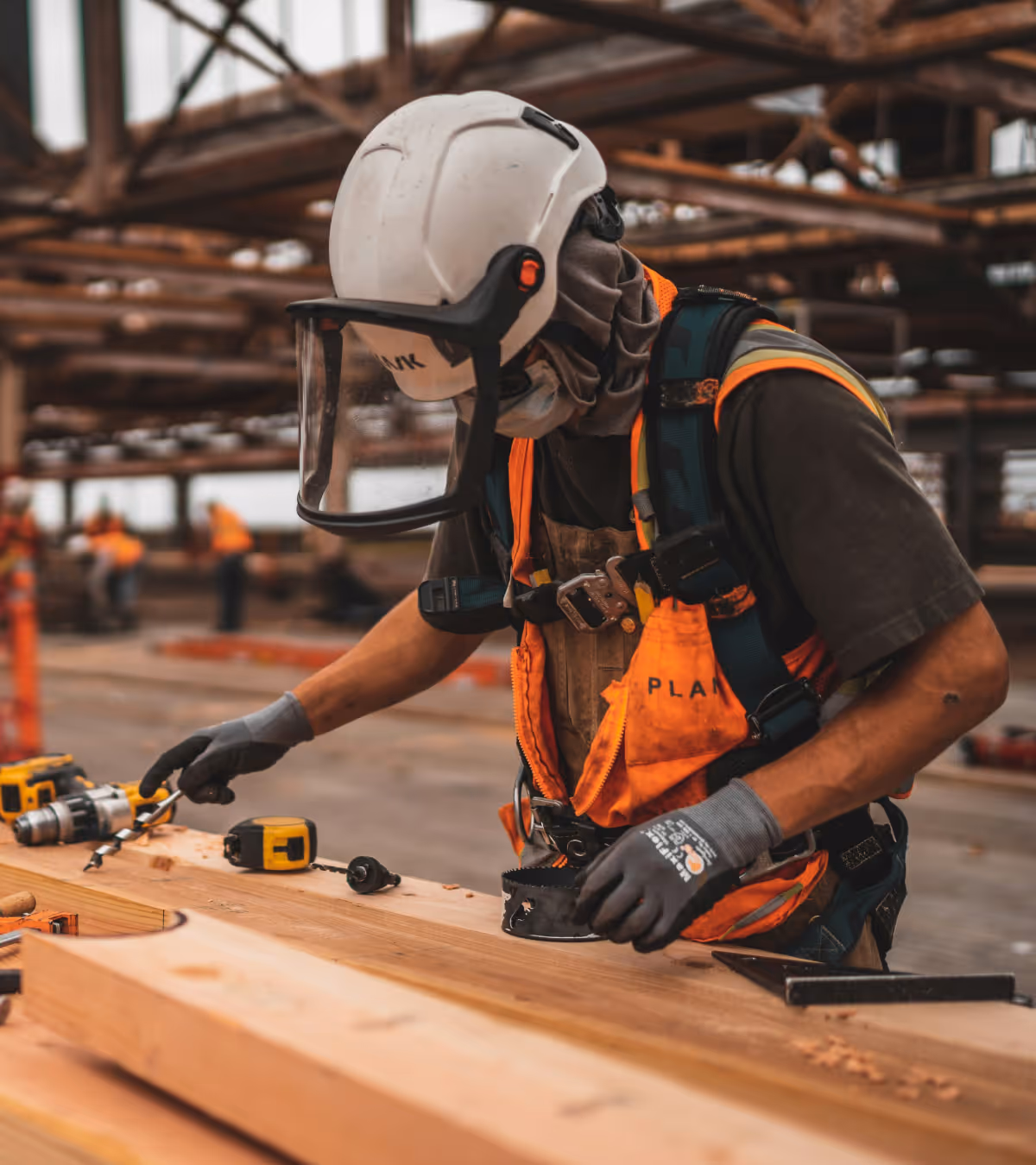 Worker in protective helmet and mask handling drill bits on a wooden plank in a construction site.